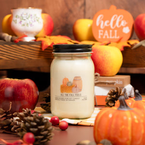 Candle labeled 'All the Fall Feels' surrounded by autumn-themed decorations including pumpkins and apples.