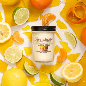 Serendipity Amber & Citrus candle jar with citrus fruits on a white background