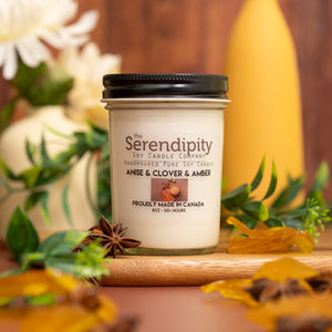 Serendipity candle with anise, clover, and amber fragrance on a wooden surface with decorative elements.