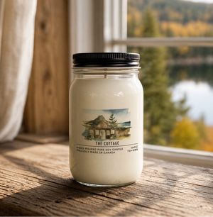 Candle jar labeled 'The Cottage' on a wooden surface with a scenic background