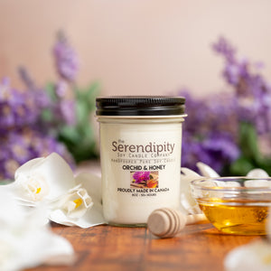 Serendipity soy candle with orchid and honey theme on a wooden surface with flowers and honeycomb in the background.