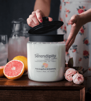 Serendipity candle jar with a person opening it, surrounded by pink grapefruit and flowers.