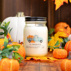 Candle labeled 'The Pumpkin Patch' surrounded by pumpkins and autumn leaves on a wooden surface.