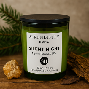 Green candle with a black lid labeled 'Serendipity Home Silent Night' on a wooden surface with natural elements.