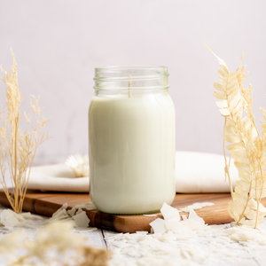 Glass jar of scented soy candle on a wooden board with decorative elements on a light background
