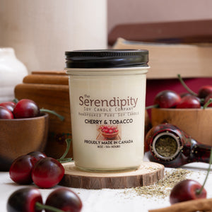 Candle from Serendipity Soy Candle Company with cherry and tobacco scent on a wooden surface with cherries and spices.