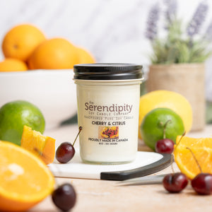 Serendipity candle with cherry and citrus theme on a wooden surface with fruits and plants.