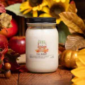 Jar candle labeled 'Fall Market' surrounded by autumn-themed decorations on a wooden surface.