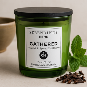 Green candle labeled 'Gathered' by Serendipity Home with mint leaves and spices on a neutral background
