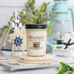 Serendipity candle labeled 'Lake House' on a surface with decorative items in the background