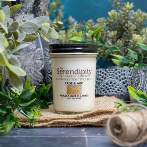 Serendipity candle with 'Sage & Mint' fragrance on a decorative surface with plants