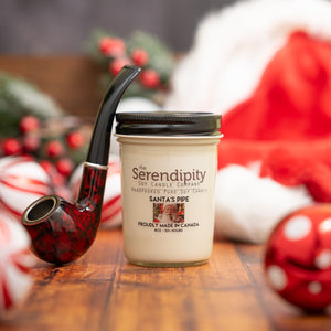 Serendipity candle with a Santa-themed pipe on a wooden surface with Christmas decorations.